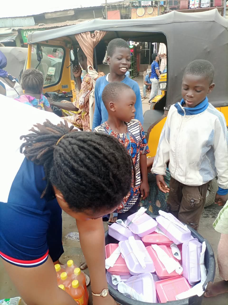 Children waiting around a basin of packed hot meals at a street distribution